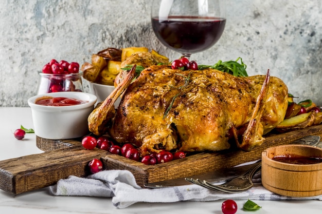 Navidad, comida de acción de gracias, pollo asado al horno con arándanos y hierbas, servido con verduras fritas, vino de bayas frescas y salsas en una mesa de mármol blanco, espacio de copia