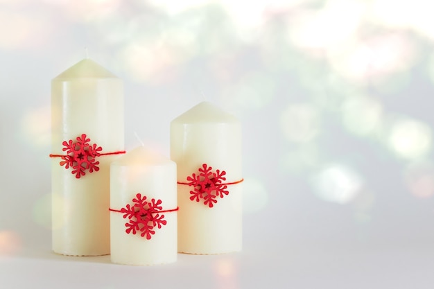 Navidad, composición de año nuevo con tres velas blancas y copos de nieve de madera roja sobre fondo blanco. Foto con copia espacio en blanco.