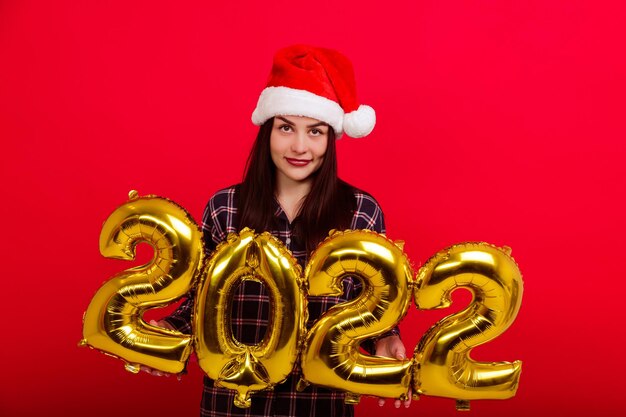 Navidad, concepto de unas felices vacaciones: una mujer joven en pijama y un gorro de Papá Noel tiene los números 2022