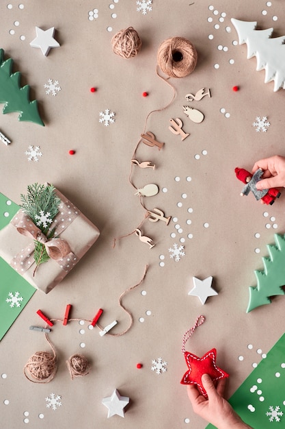 Navidad sin desperdicio, plano sobre fondo de papel artesanal: guirnalda de muñecas textiles, caja de regalo envuelta, manos femeninas con muñeca y estrella textil roja. Alternativa ecológica Navidad verde.