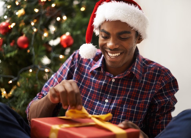 La Navidad es mi época favorita del año Fotografía de un apuesto joven desenvolviendo su regalo de Navidad