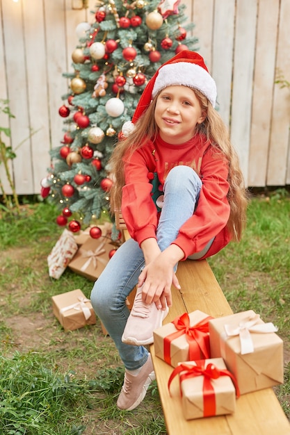 Navidad familiar en julio. Retrato de niña cerca del árbol de Navidad con regalos. Pino de decoración de bebé. Concepto de personas y vacaciones de invierno. Feliz Navidad y felices fiestas tarjeta de felicitación. Niño de navidad