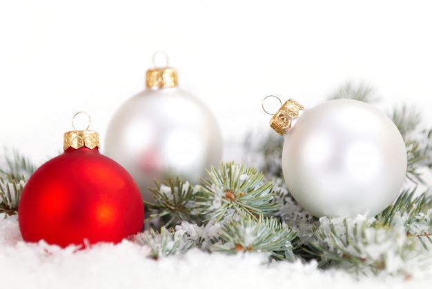 Navidad hermosas bolas blancas y rojas con rama de abeto y nieve sobre fondo blanco.