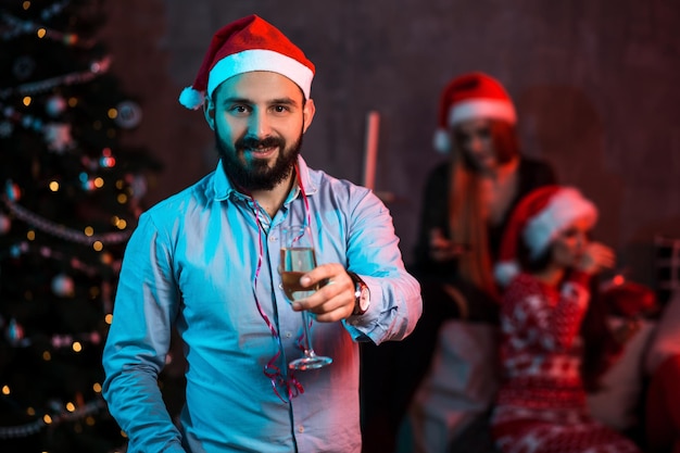 Navidad, Navidad, año nuevo, invierno, concepto de felicidad - hombre sonriente con sombrero de ayudante de santa con una copa de champán