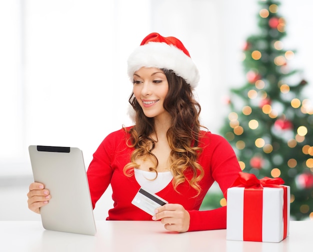 Navidad, Navidad, concepto de compras online - mujer con sombrero de ayudante de santa con caja de regalo, tablet pc y tarjeta de crédito