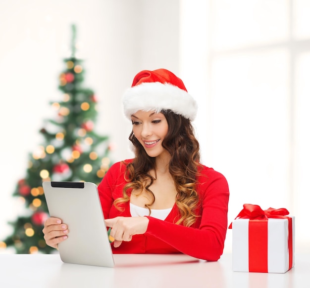 Navidad, Navidad, concepto de compras online - mujer con sombrero de ayudante de santa con caja de regalo y tablet pc