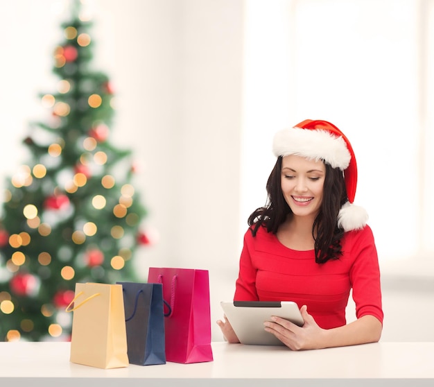 Navidad, Navidad, concepto de compras online - mujer con sombrero de ayudante de santa con caja de regalo y tablet pc