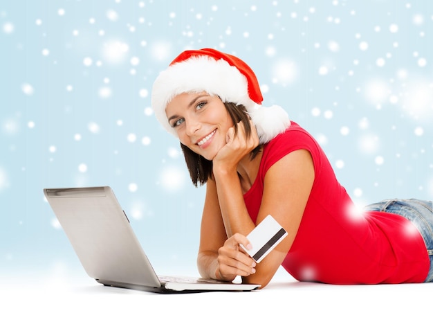 Navidad, Navidad, concepto de compras online - mujer con sombrero de ayudante de santa con ordenador portátil y tarjeta de crédito