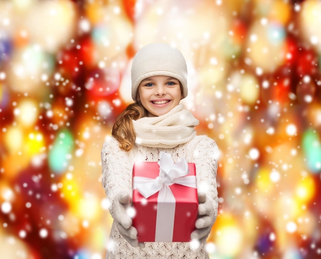 navidad, navidad, concepto de felicidad - niña sonriente con sombrero, silenciador y guantes con caja de regalo