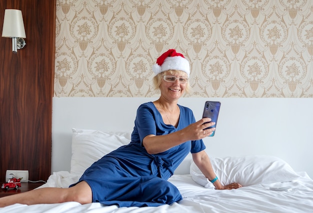 Navidad, Navidad, concepto de saludos en línea - una mujer con un sombrero de ayudante de Santa Claus con un teléfono inteligente.