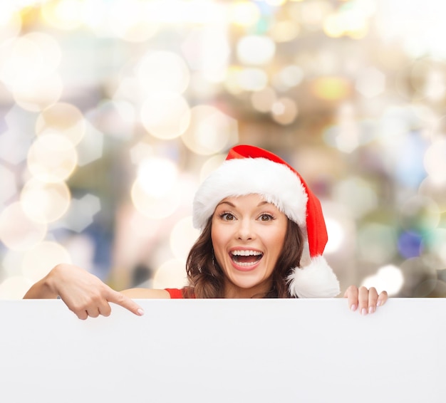 navidad, navidad, gente, publicidad y concepto de venta - mujer feliz con sombrero de ayudante de santa con pizarra en blanco sobre fondo de luces