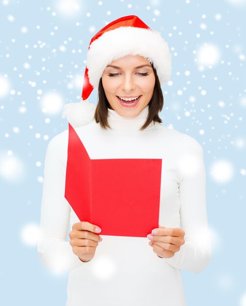 Navidad, Navidad, gente, publicidad, concepto de venta - mujer feliz con sombrero de ayudante de santa con postal roja en blanco