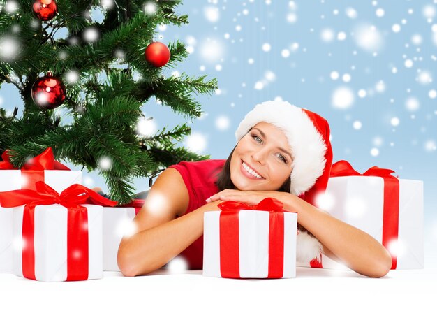 Navidad, Navidad, invierno, concepto de felicidad - mujer sonriente con sombrero de ayudante de santa con muchas cajas de regalo y árbol