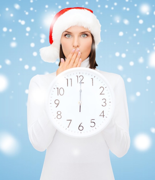Navidad, Navidad, invierno, concepto de felicidad - mujer sonriente con sombrero de ayudante de santa con reloj mostrando 12