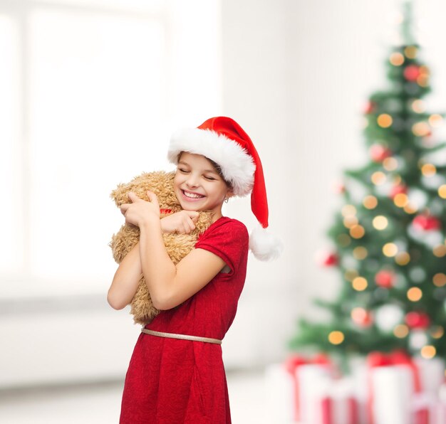 Navidad, Navidad, invierno, concepto de felicidad - niña sonriente con sombrero de ayudante de santa con osito de peluche