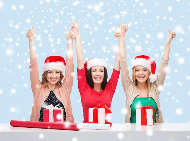 Navidad, Navidad, invierno, concepto de felicidad - tres mujeres sonrientes con sombreros de ayudante de santa con cajas de regalo