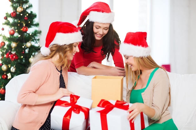 Navidad, Navidad, invierno, concepto de felicidad: tres mujeres sonrientes con sombreros de ayudante de santa con muchas cajas de regalo