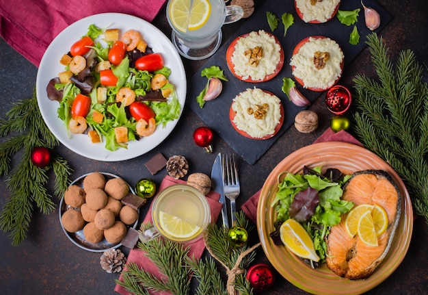 Navidad o año nuevo concepto de mesa de cena familiar con decoración de vacaciones. Delicioso filete asado de salmón, ensalada, aperitivos y postre en la mesa de piedra oscura. Vista superior