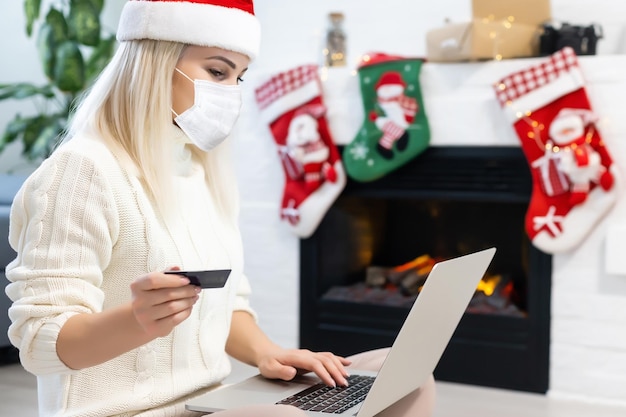 Navidad con pandemia de coronawirus. Retrato de una mujer joven con mascarilla protectora y que se ve triste por Covid-19 con árbol de Navidad en el fondo, coronavirus y concepto de Navidad.