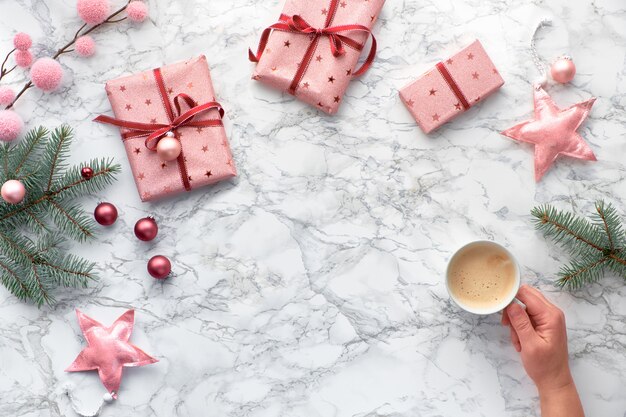 Navidad plana yacía sobre mesa de mármol con espacio de copia. Mano que sostiene la taza de café. Decoraciones de invierno: ramas de abeto, estrellas suaves y baratijas rosas