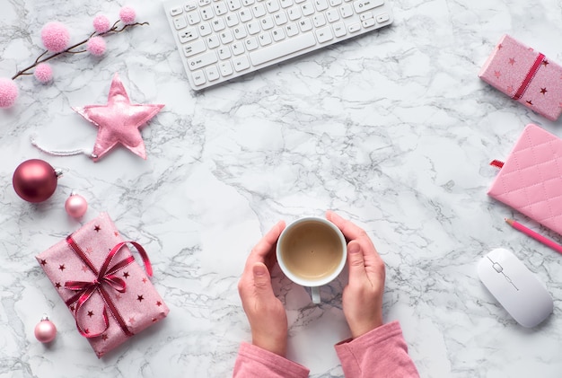 Navidad plana yacía sobre la mesa de mármol. Manos calentando de una taza de café caliente. Ramitas de abeto, estrellas suaves y baratijas rosas, espacio de copia