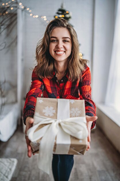 Navidad. Pretty Woman en camisa y calcetines caminando en casa con caja de regalo de Navidad, árbol de Navidad detrás