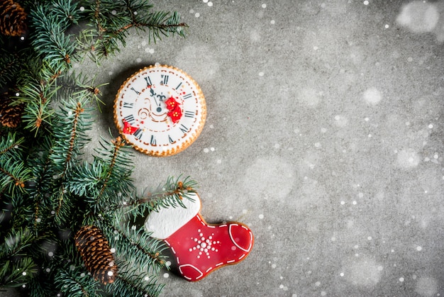 Navidad con rama de abeto, galletas de jengibre coloridas caseras, conos de pino y decoraciones en la mesa de piedra gris.