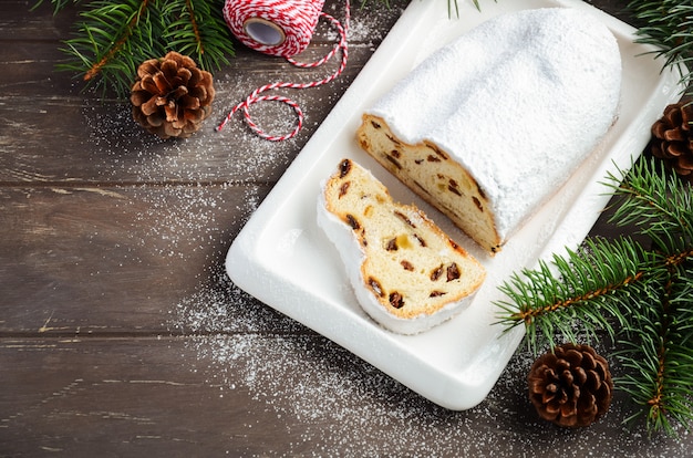 Navidad Stollen. Postre festivo tradicional alemán, europeo en la mesa de madera vieja. Concepto de vacaciones decorado con ramas de abeto y conos.