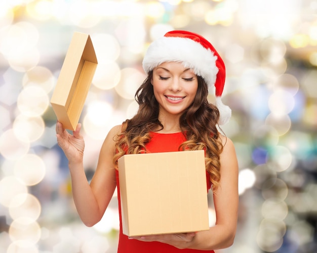 Foto navidad, vacaciones, celebración y concepto de la gente - mujer sonriente con sombrero de ayudante de santa con caja de regalo sobre fondo de luces