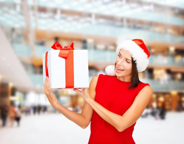 navidad, vacaciones, celebración y concepto de la gente - mujer sonriente vestida de rojo con caja de regalo sobre el fondo del centro comercial