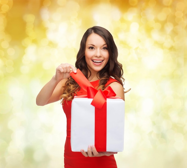 navidad, vacaciones, día de san valentín, celebración y concepto de la gente - mujer sonriente vestida de rojo con caja de regalo sobre fondo de luces amarillas