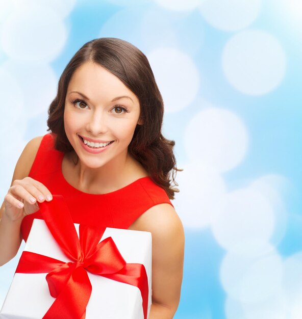 navidad, vacaciones, día de san valentín, celebración y concepto de la gente - mujer sonriente vestida de rojo con caja de regalo sobre fondo de luces azules