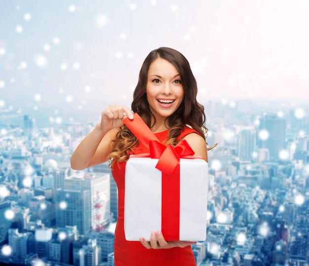 navidad, vacaciones, día de san valentín, celebración y concepto de la gente - mujer sonriente vestida de rojo con caja de regalo sobre el fondo nevado de la ciudad