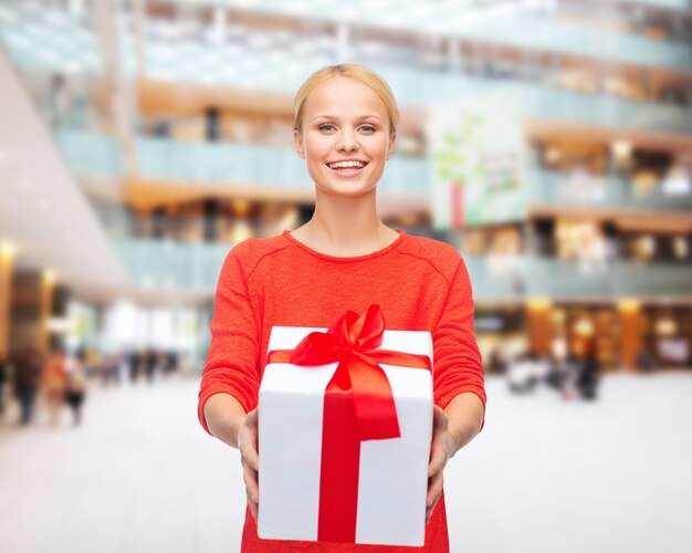 navidad, vacaciones, día de san valentín, compras y concepto de personas - mujer sonriente vestida de rojo con caja de regalo sobre fondo de luces