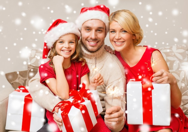 navidad, vacaciones, felicidad y concepto de la gente - familia sonriente en sombreros de ayudante de santa con muchas cajas de regalo y bengalas en casa