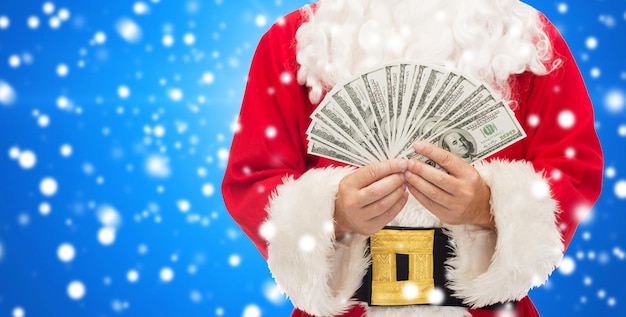 navidad, vacaciones, ganar, moneda y concepto de personas - cerca de santa claus con dinero en dólares sobre fondo azul nevado