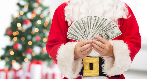 navidad, vacaciones, ganar, moneda y concepto de personas - cerca de santa claus con dinero en dólares sobre la sala de estar con árbol