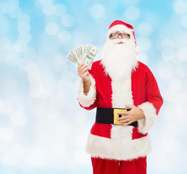 navidad, vacaciones, ganar, moneda y concepto de personas - hombre disfrazado de santa claus con dinero en dólares sobre fondo de luces azules