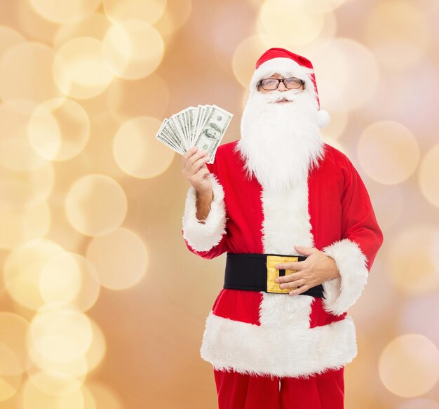 navidad, vacaciones, ganar, moneda y concepto de personas - hombre disfrazado de santa claus con dinero en dólares sobre fondo de luces beige