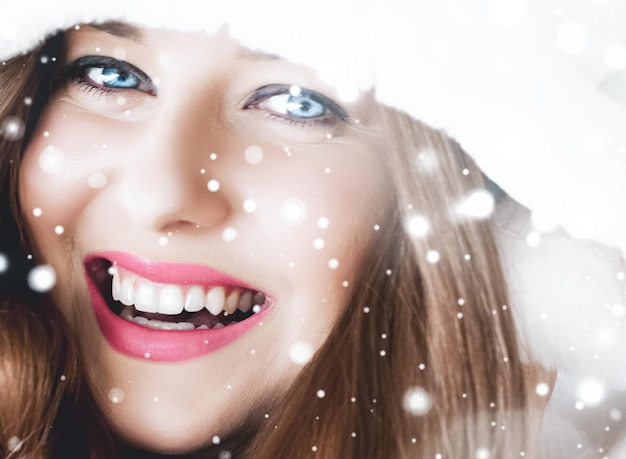 Foto navidad y vacaciones de invierno retrato de mujer joven en abrigo de piel con capucha blanca nieve sobre fondo azul moda y estilo de vida