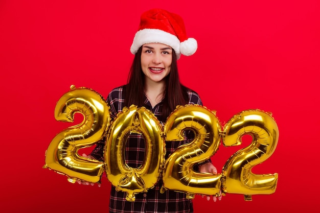 Navidad, vacaciones - una joven mujer sonriente en pijama y un gorro de Papá Noel tiene los números 2022