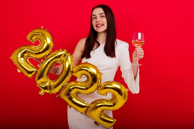 Navidad, vacaciones - una joven mujer sonriente con un vestido blanco tiene los números 2022 y una copa de vino