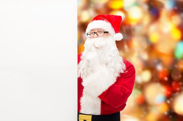 navidad, vacaciones, publicidad y concepto de la gente - hombre disfrazado de santa claus con cartelera blanca en blanco haciendo un gesto de silencio sobre el fondo de las luces rojas