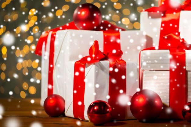 navidad, vacaciones, regalos, año nuevo y concepto de celebración - cierre de cajas de regalo y bolas rojas en el suelo de madera sobre fondo de luces
