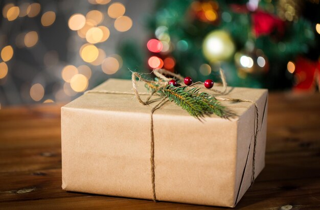 navidad, vacaciones, regalos, año nuevo y concepto de decoración - cierre de caja de regalo envuelto en papel de correo marrón y decorado con brunch de abeto y lazo de cuerda sobre fondo de luces