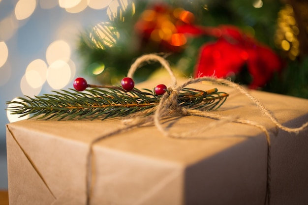 navidad, vacaciones, regalos, año nuevo y concepto de decoración - cierre de caja de regalo envuelto en papel de correo marrón y decorado con brunch de abeto y lazo de cuerda sobre fondo de luces
