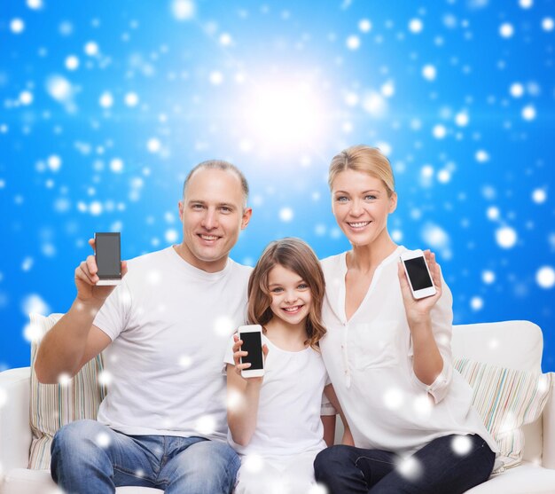 navidad, vacaciones, tecnología, publicidad y concepto de personas - familia sonriente con smartphones sobre fondo azul nevado