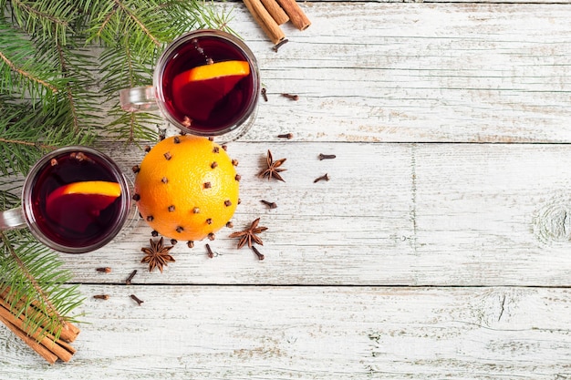 Navidad vino caliente caliente con canela, naranja y anís sobre fondo blanco de madera con árbol