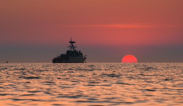 Navio de guerra militar de silhueta e o sol