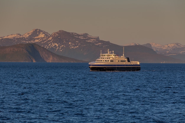 Navio navegando nas águas azuis dos fiordes noruegueses no dia polar, sol da meia-noite.